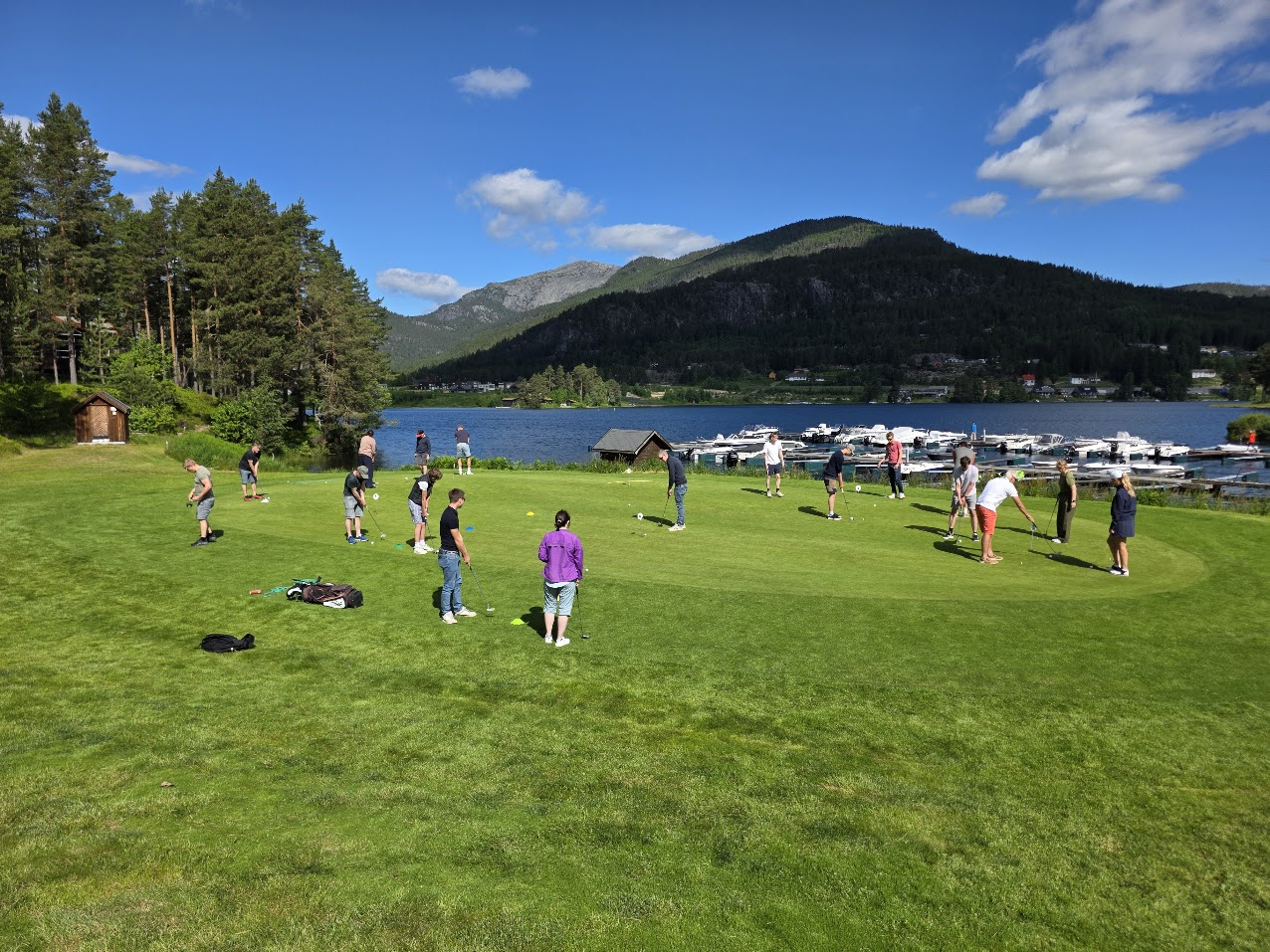 Gruppe som øver på golf ved vannet og fjellene på Vrådal Golf