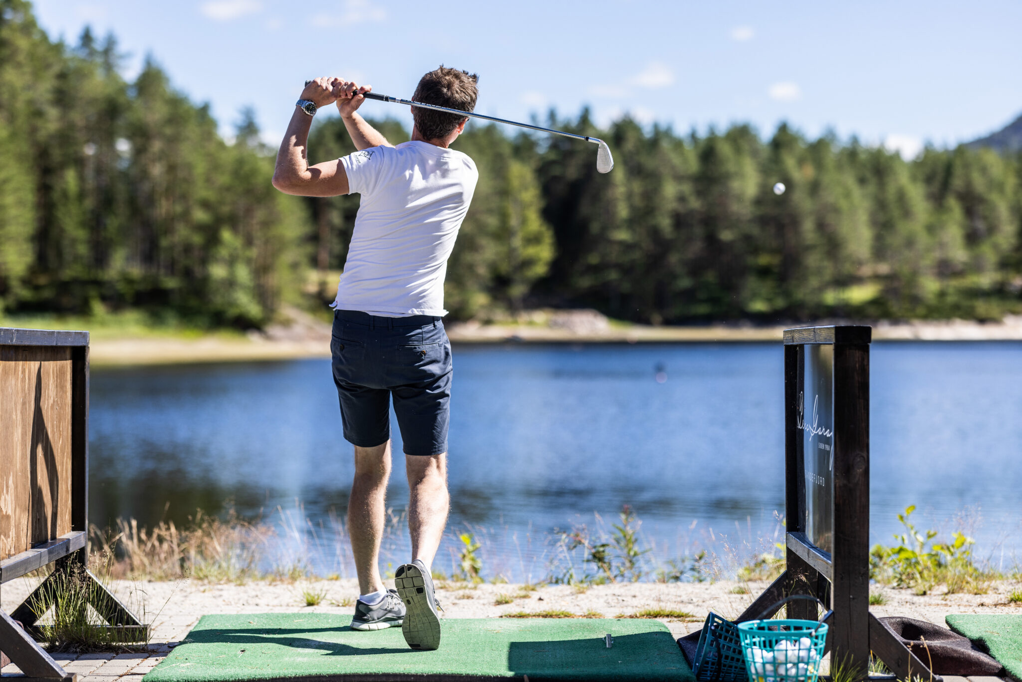 Golfspiller i avslutningen av et slag på Vrådal Golf, med skogen i bakgrunnen